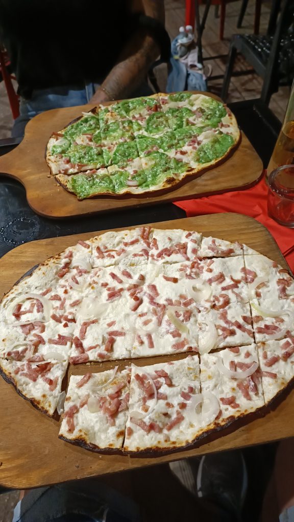 Zwei Flammkuchen auf Holzbrettern in einem Restaurant in Colmar, einer klassisch mit Speck und Zwiebeln, einer mit Basilikum und Käse