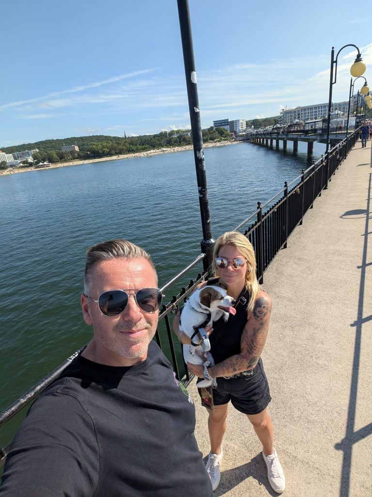 Eva und Robert machen ein Selfie auf der Seebrücke von Misdroy, Eva trägt Hund Tyson auf dem Arm