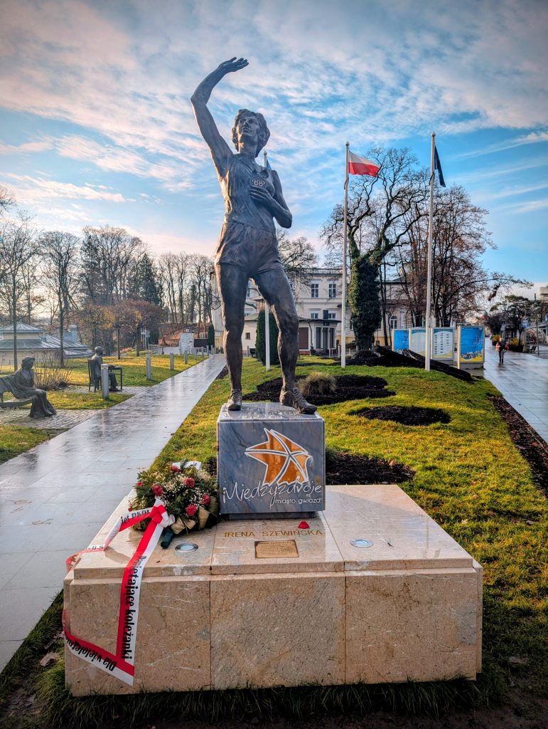 Bronzestatue der Leichtathletin Irena Szewińska mit erhobenem Arm auf einem Marmorpodest mit Blumen an der Promenade in Misdroy