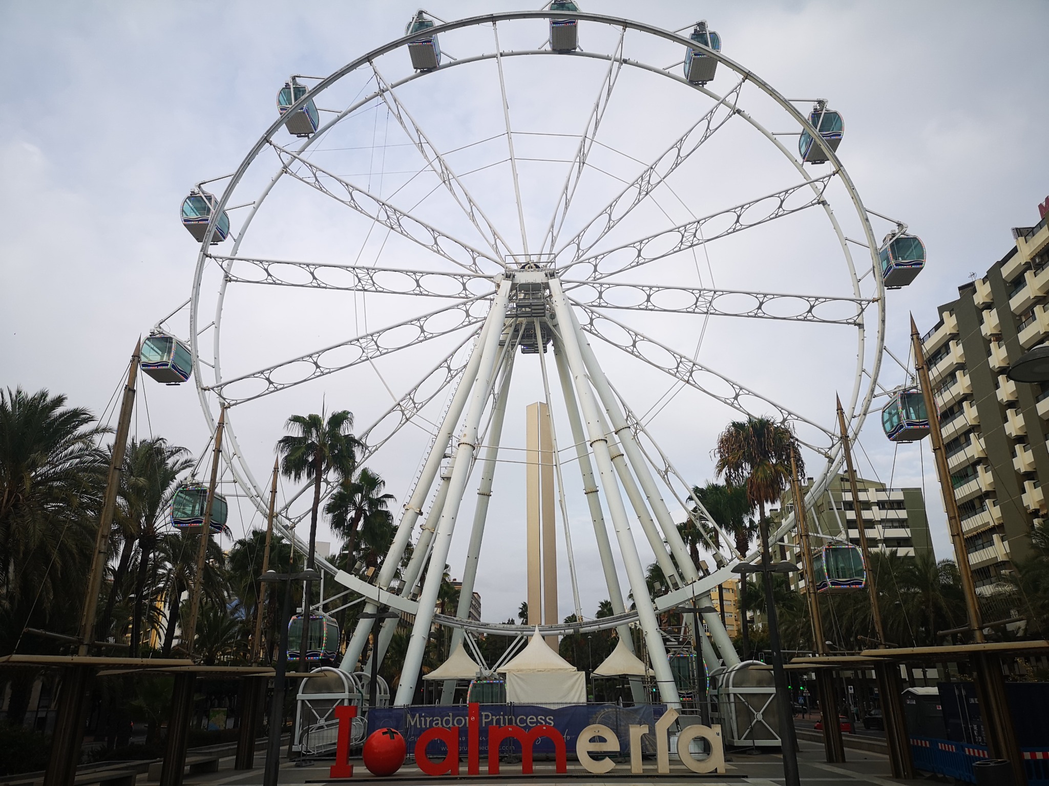 Riesenrad in Almería zwischen Palmen unter bewölktem Himmel