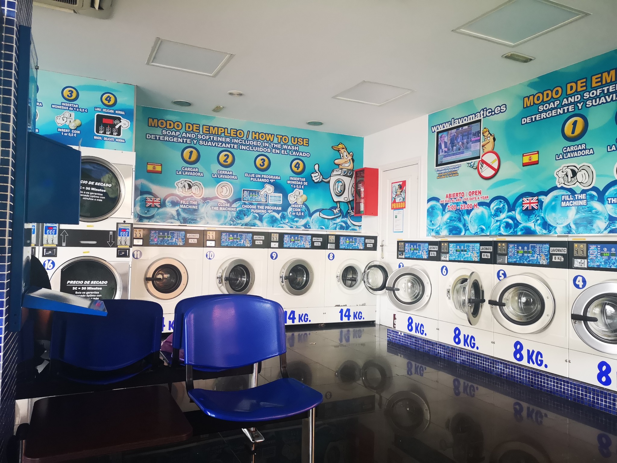Waschmaschinen und blaue Stühle im Selbstbedienungs-Waschsalon Lavomatic in Almería