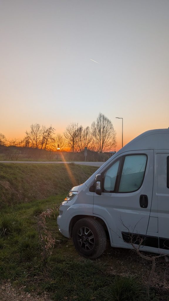 Front unseres Campers vor Bäumen und Abendhimmel im Jura