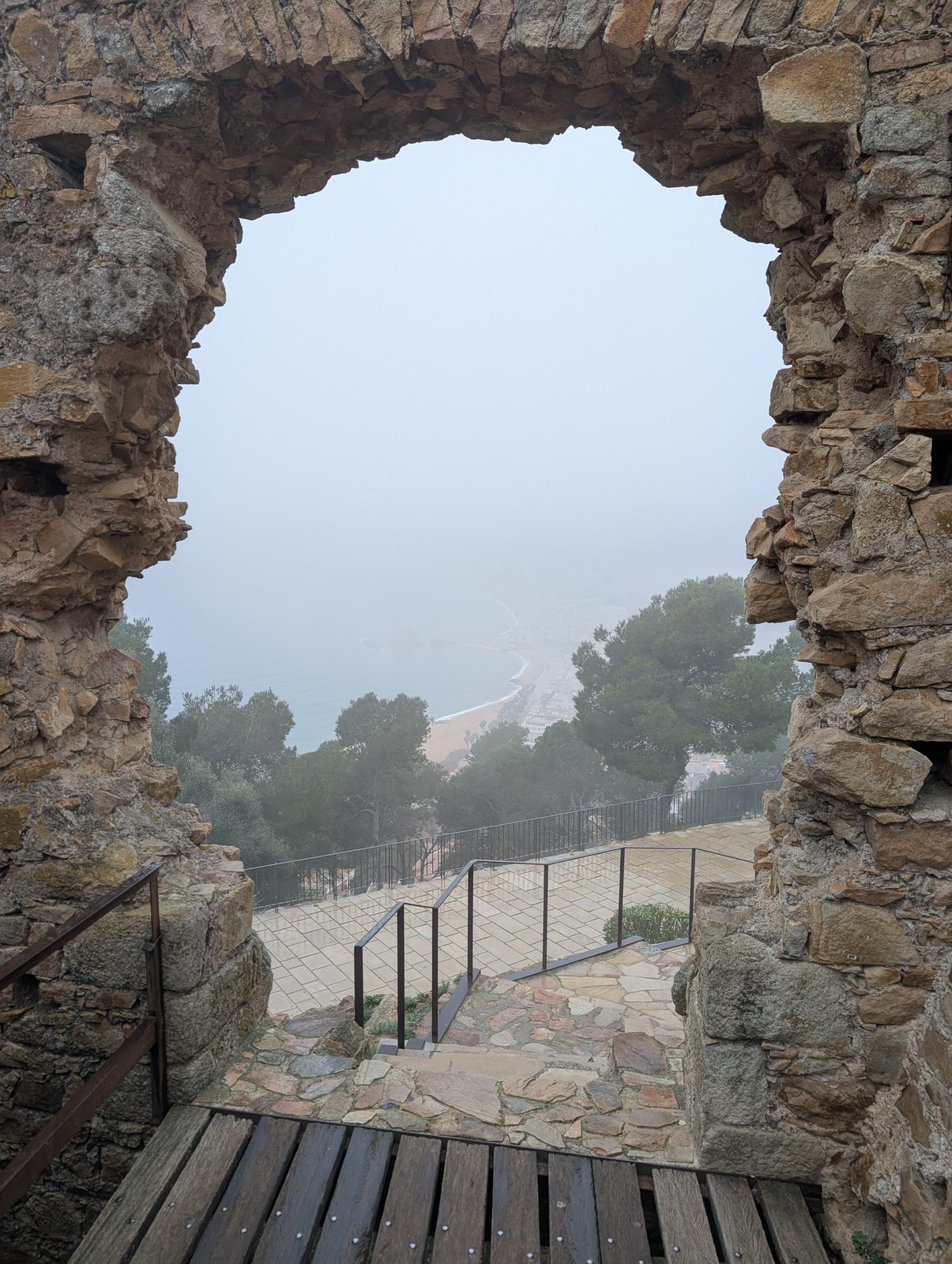 Blick durch einen Mauerdurchbruch des Castell de Sant Joan auf die neblige Bucht von Blanes