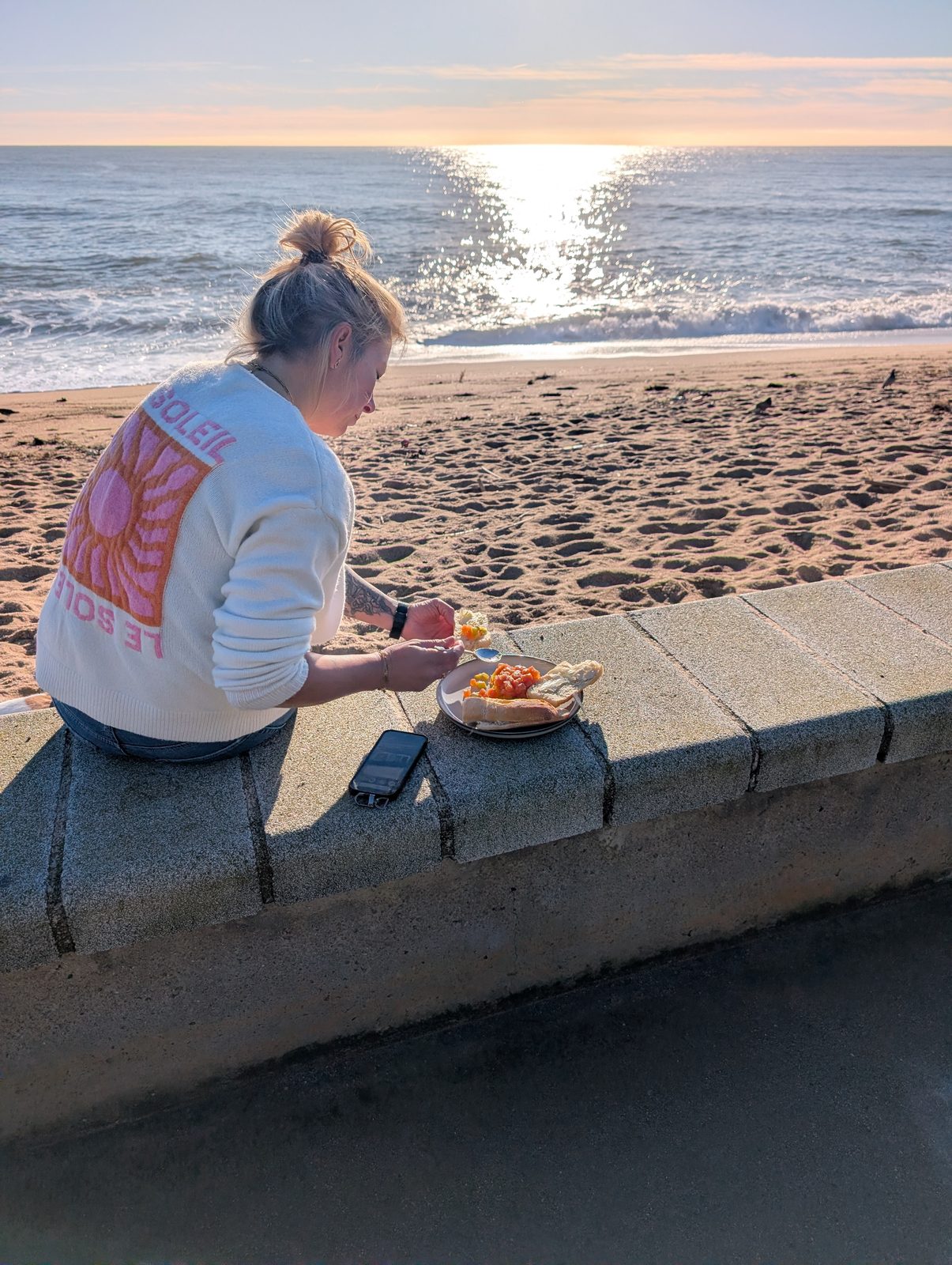Frühstücksteller auf der Strandmauer von Blanes, dahinter Strand und Meer im Morgenlicht