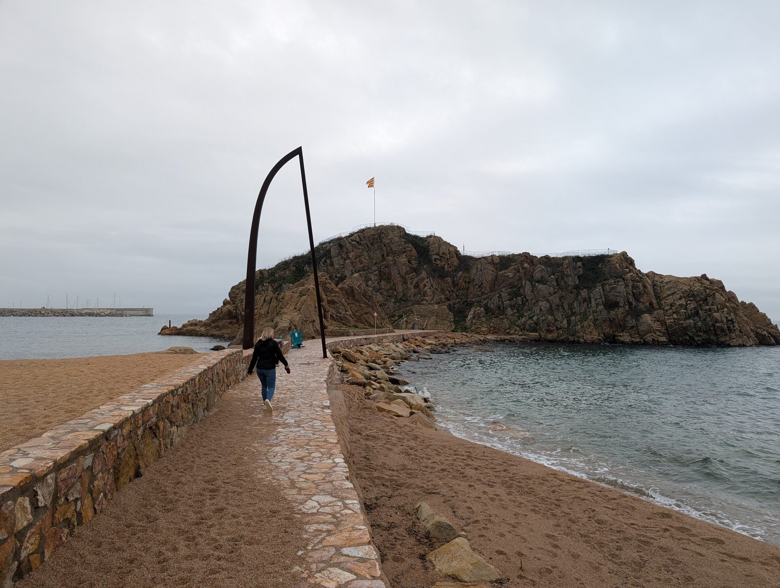 Der Felsen Sa Palomera in Blanes bei Regen, im Vordergrund der leere Sandstrand