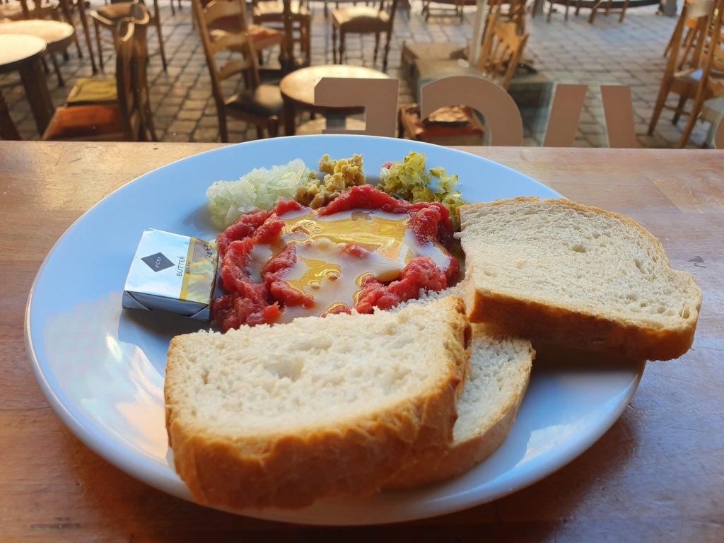 Polnisches Tatar mit rohem Eigelb, Zwiebeln und Gurken auf einem Teller, dazu Weißbrot