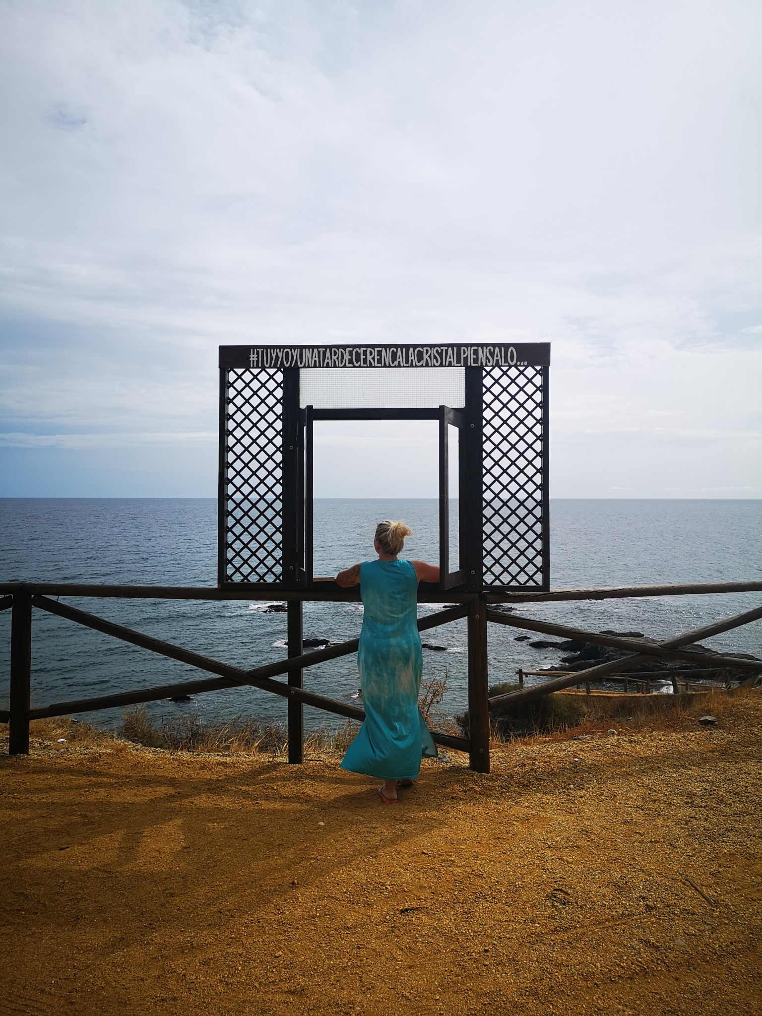 Eva vor einem Fensterrahmen mit dem Spruch „Tú y yo y una tarde en Cala Cristal“ über dem Meer