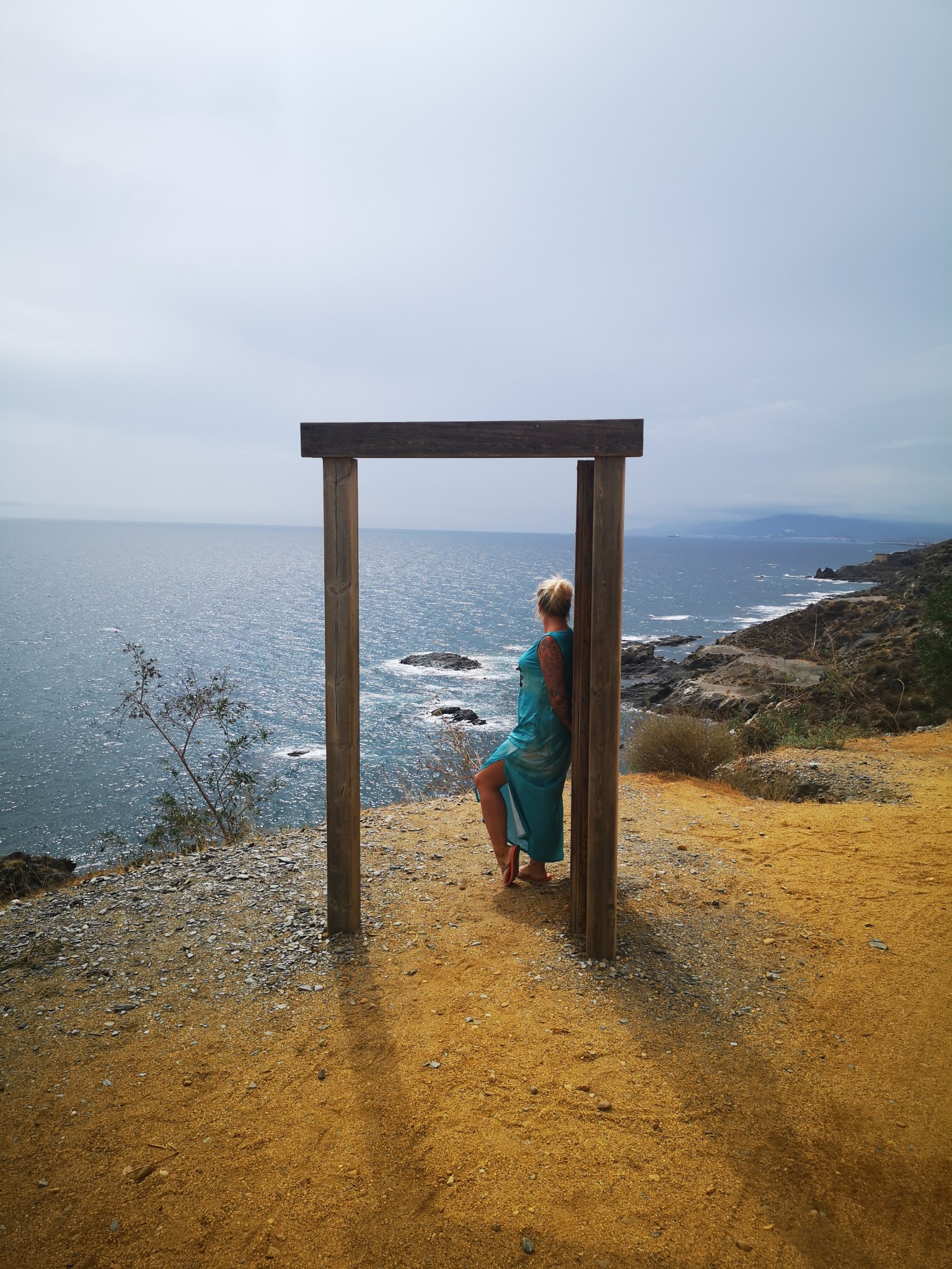 Eva lehnt in einem hohen Holzrahmen an der Klippe über dem Meer an der Cala Cristal