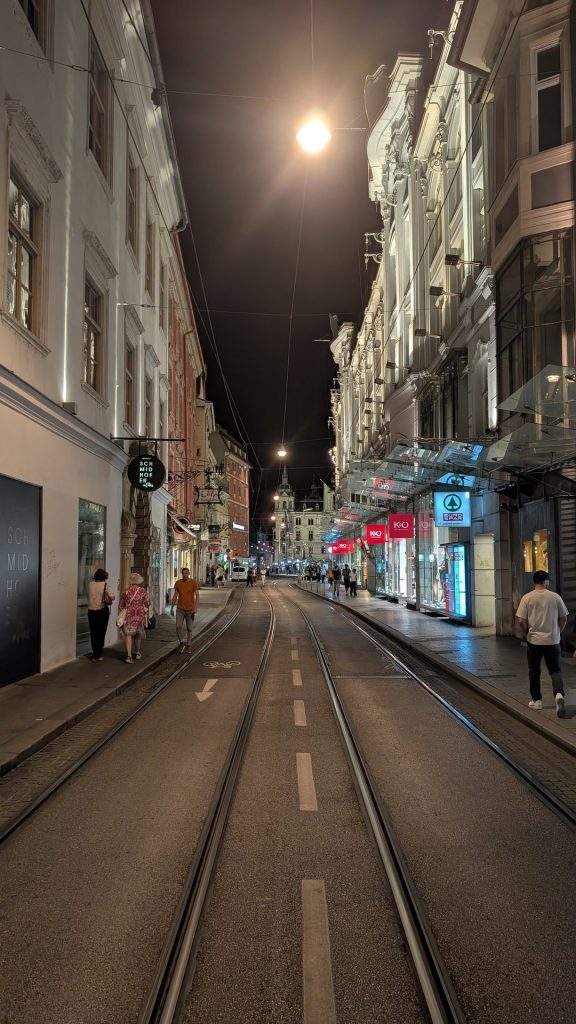 Nächtliche Altstadtgasse in Graz mit Straßenbahnschienen und Mond
