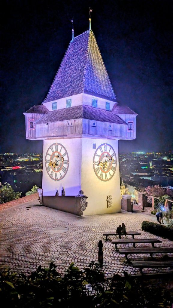 Der beleuchtete Grazer Uhrturm bei Nacht