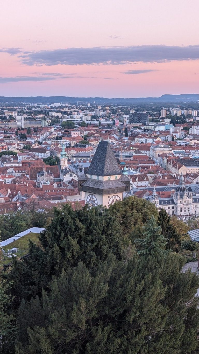 Der Grazer Uhrturm von oben mit der Altstadt und rosa Abendhimmel