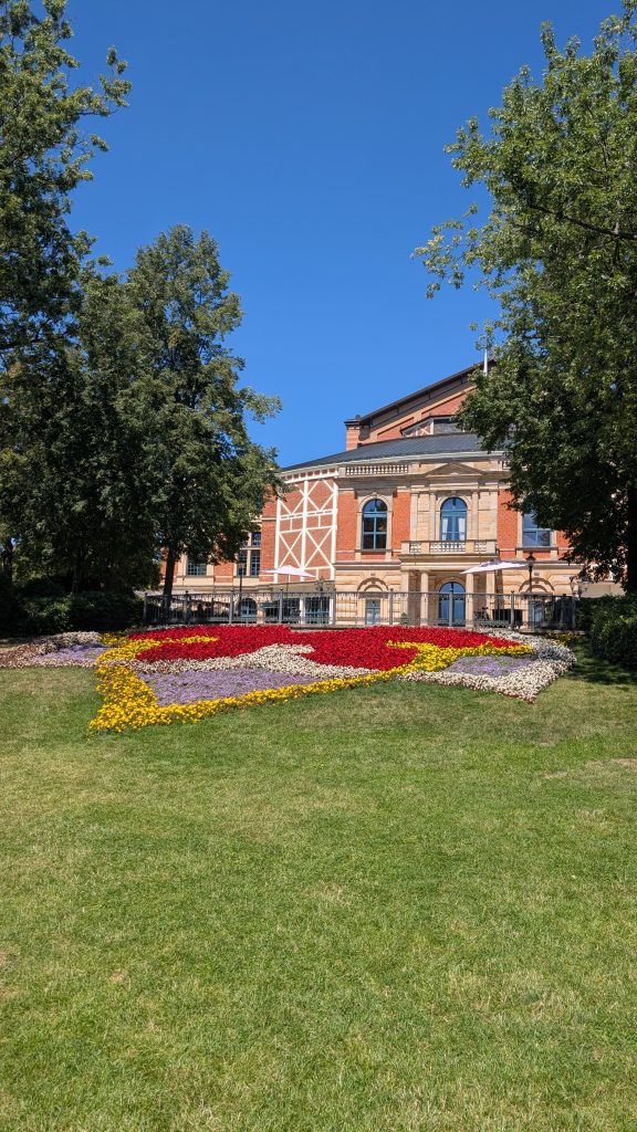Festspielhaus Bayreuth von außen mit Blumenbeet im Wagner-Design