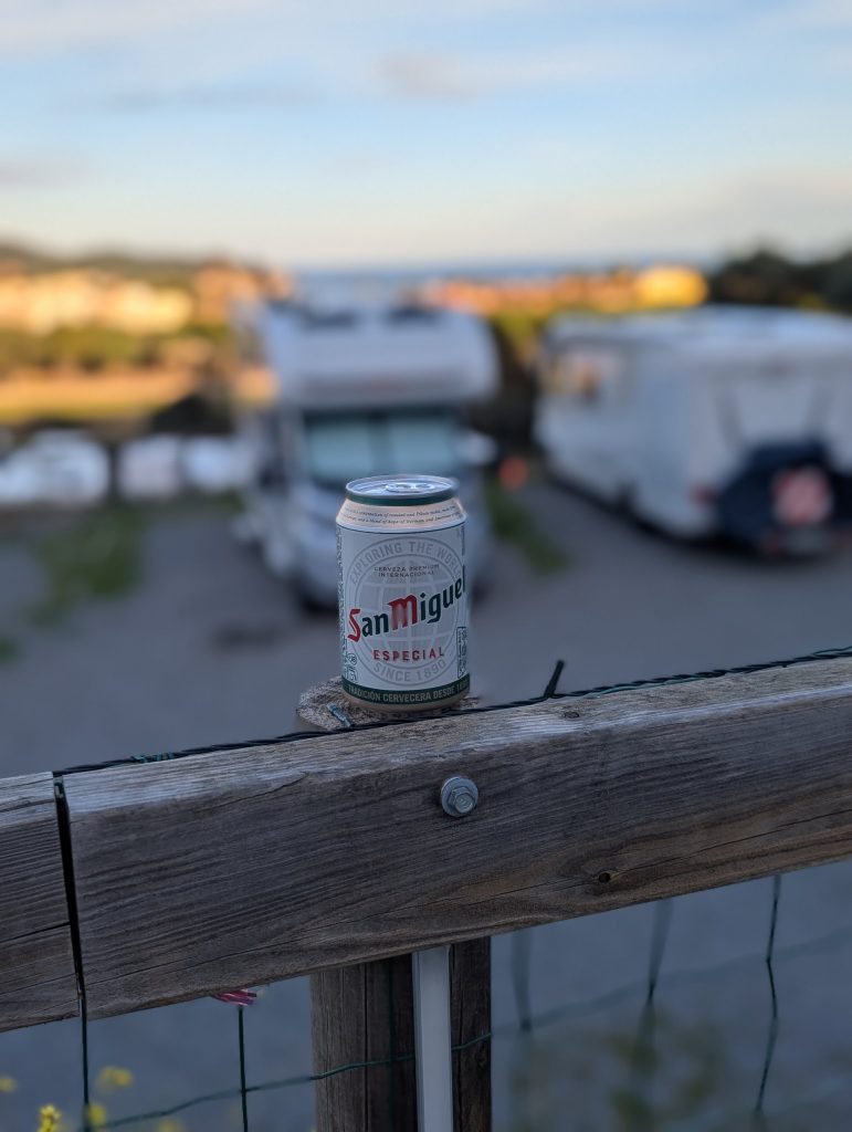 Dose San Miguel auf dem Holzzaun am Stellplatz Autocaravaning Palamós, dahinter Wohnmobile und das Meer am späten Nachmittag