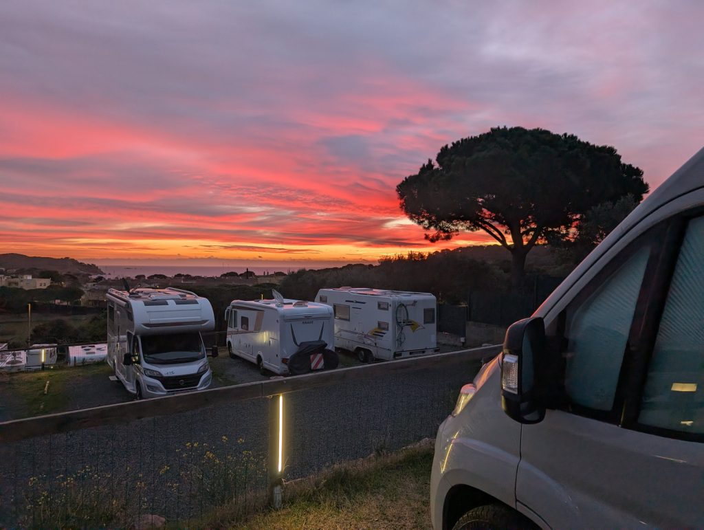 Wohnmobile auf dem Stellplatz Autocaravaning Palamós bei rotem Morgenhimmel, Pinie als Silhouette