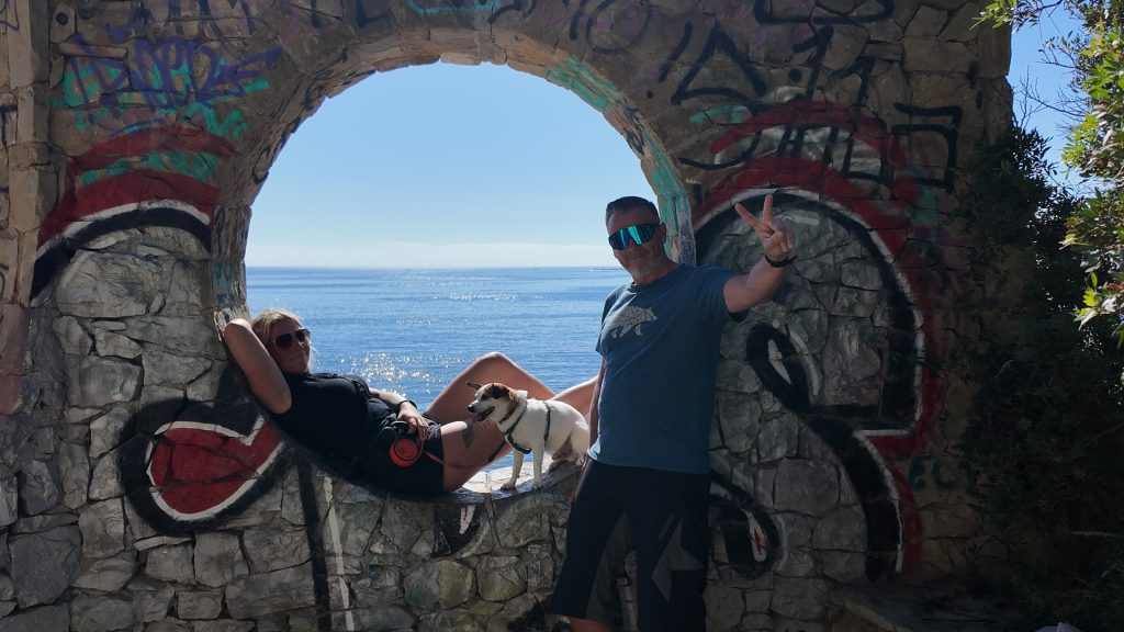 Eva liegt mit Tyson im runden Fenster der Social-Club-Ruine bei Calp, Robert steht daneben, dahinter das Mittelmeer