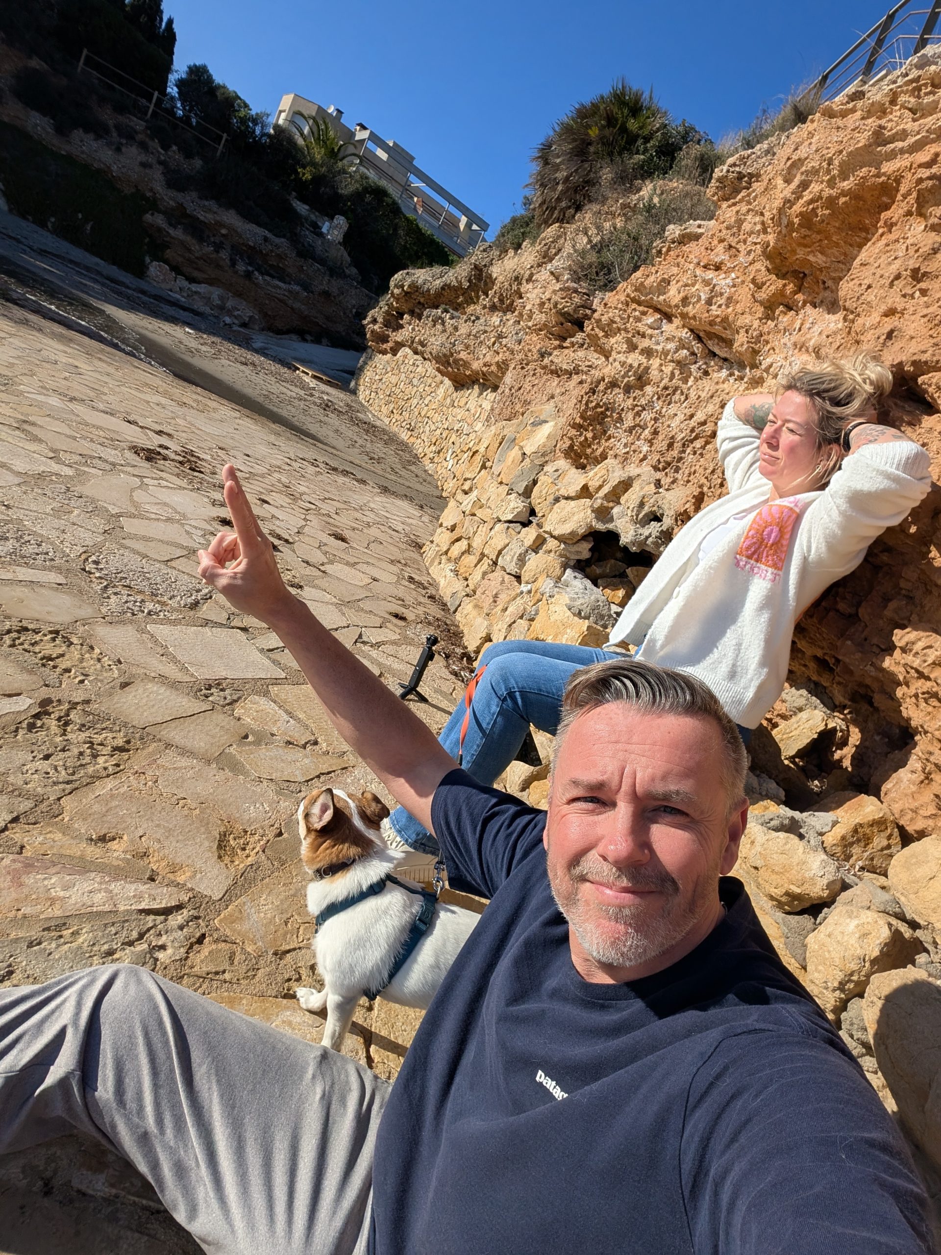 Robert macht ein Selfie an der Cala Pepo, Eva liegt dahinter in der Sonne auf den Felsen, Tyson daneben