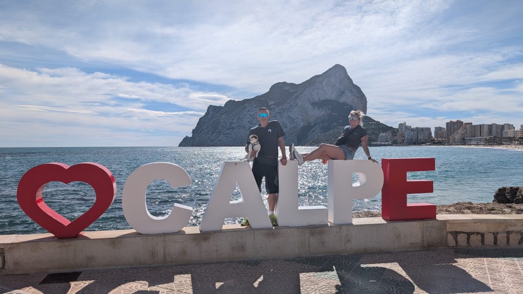 Robert mit Tyson auf dem Arm und Eva auf dem roten Herz-CALPE-Schriftzug am Meer, dahinter der Peñón d'Ifach